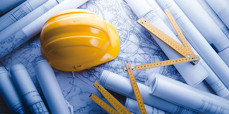 کلاه مهندسی و ابزار طراحی روی میز، نشان‌دهنده بررسی تأثیر ساختمان‌های هوشمند بر کاهش مصرف انرژی